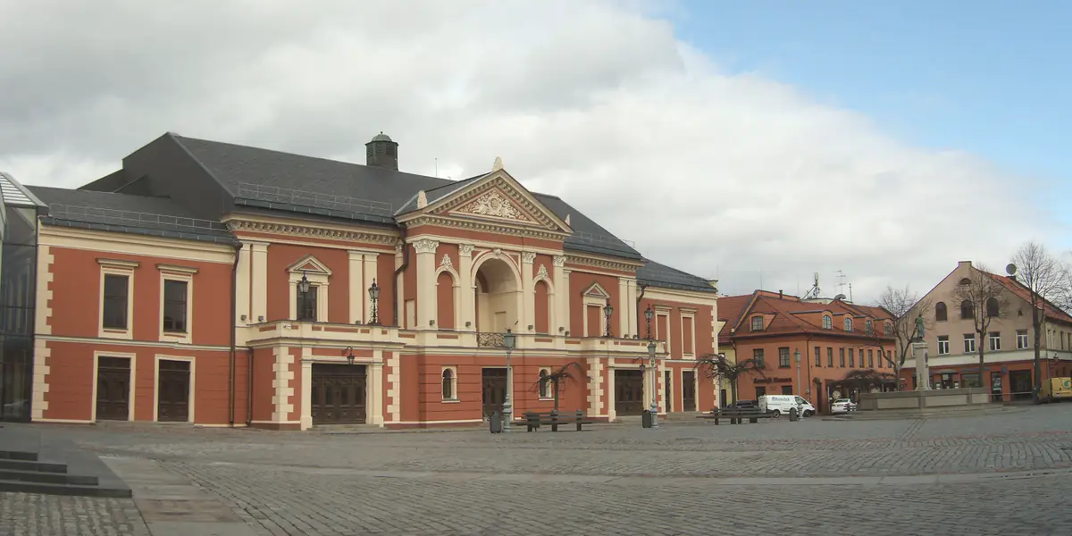 Raudonų plytų ir šviesaus tinko Klaipėdos dramos teatro pastatas su portiku; priešais – grįsta Teatro aikštė, dešiniau – senamiesčio namai.