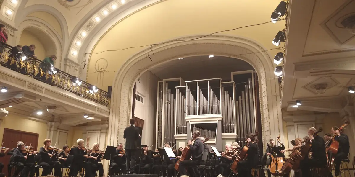 Lietuvos nacionalinės filharmonijos Didžioji salė per koncertą: orkestras scenoje priešais vargonus, virš scenos – arka, kairėje – balkonas su publika.